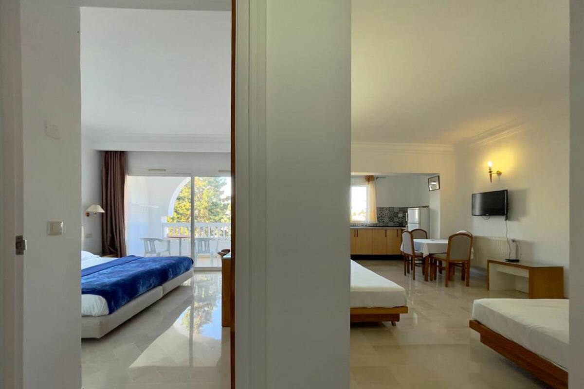 Habitación de hotel con balcón, kitchenette y televisor.