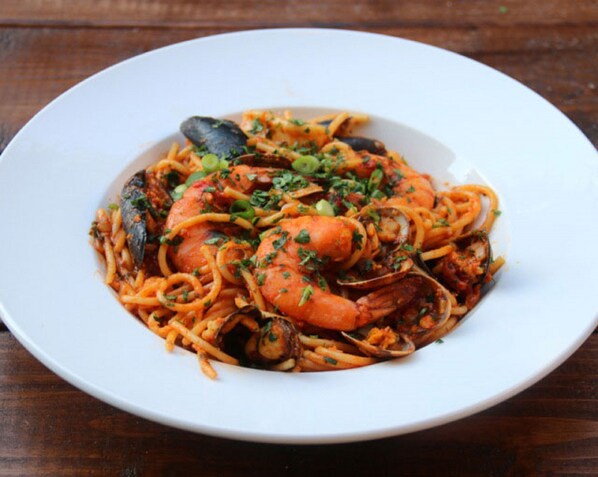 Une assiette de pâtes aux fruits de mer, avec des crevettes et des moules, garnie d’herbes aromatiques.