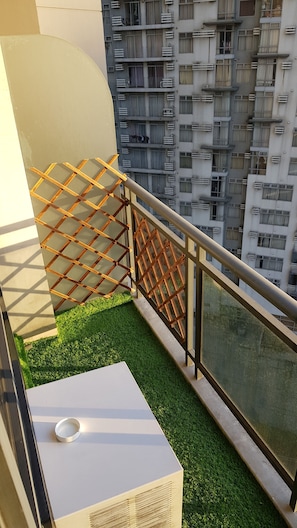 A balcony with a metal railing, a small patch of artificial grass, and a white table with a circular object on it.