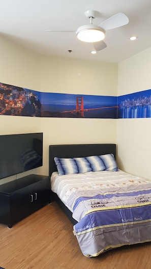 A bedroom with a bed, a TV, a ceiling fan, and two large wall art pieces depicting the Golden Gate Bridge.