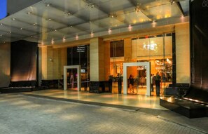 A modern hotel entrance with glass doors, a reception area, and a visible signboard.