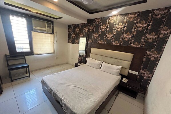 A bedroom with a bed, a nightstand, a chair, and a window with blinds.