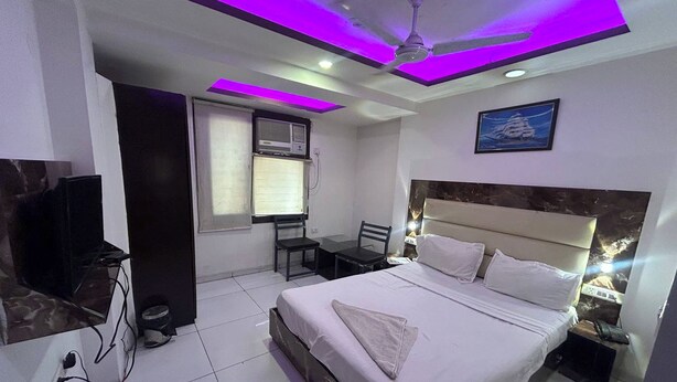A hotel room with a bed, a desk, a chair, a television, and a ceiling fan.