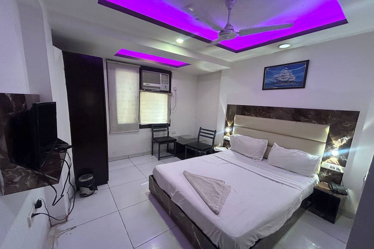 Una habitación de hotel con cama, escritorio, silla, televisor y ventilador de techo.