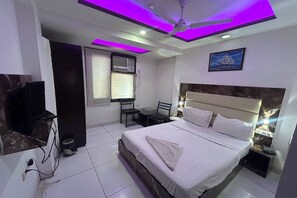 A hotel room with a bed, a desk, a chair, a television, and a ceiling fan.