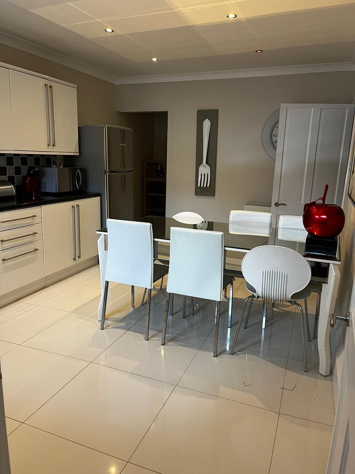 Een moderne keuken met witte kasten, een eettafel met vier stoelen, en een rode appel op het aanrecht.