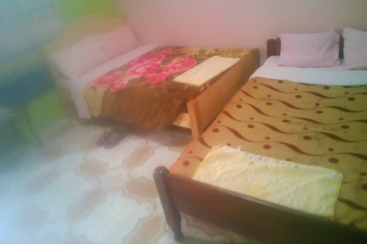 A room with two beds, one with a floral bedspread and the other with a patterned bedspread. There is a chair in the foreground.