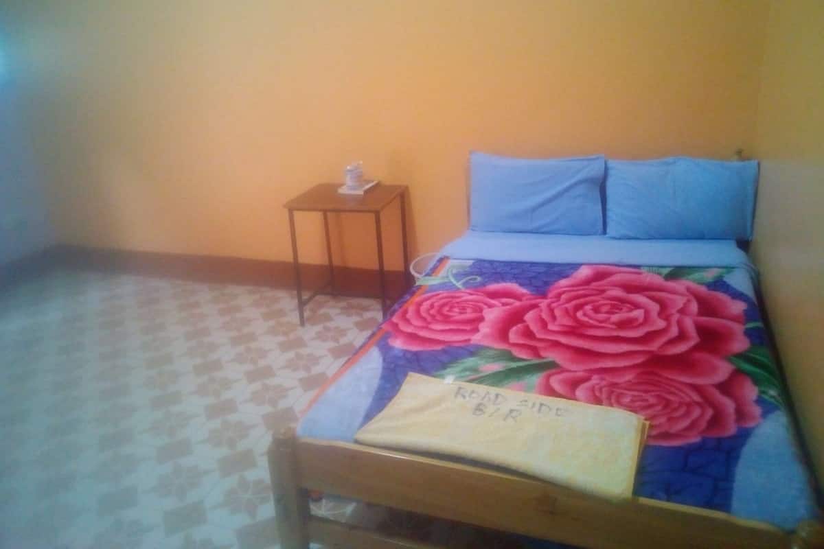 A single bed with a floral bedspread, a small bedside table with a lamp, and a wall with a door.