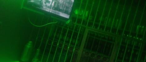 Una habitación con una pantalla iluminada en verde mostrando un mapa, una baranda metálica y una botella de agua sobre una mesa.