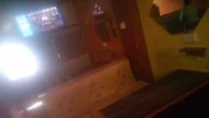 Una habitació amb poca llum, amb un sofà blanc i una banca de fusta. Un televisor està fixat a la paret.