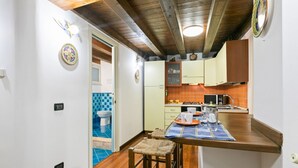 A compact kitchen with a blue tiled backsplash, wooden ceiling beams, and a small dining area with stools.