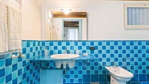 A bathroom with blue-tiled walls, a sink, a bidet, and a mirror.