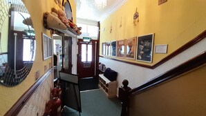 A hallway with a staircase, a fire extinguisher, a wall-mounted shelf with stuffed animals, and framed pictures. - Starlight Guest House (Blackpool)