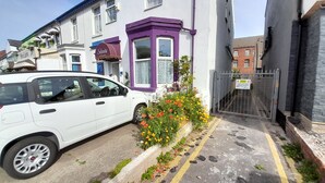 A white car parked on a narrow street with a purple house and a flower bed in front. - Starlight Guest House (Blackpool)