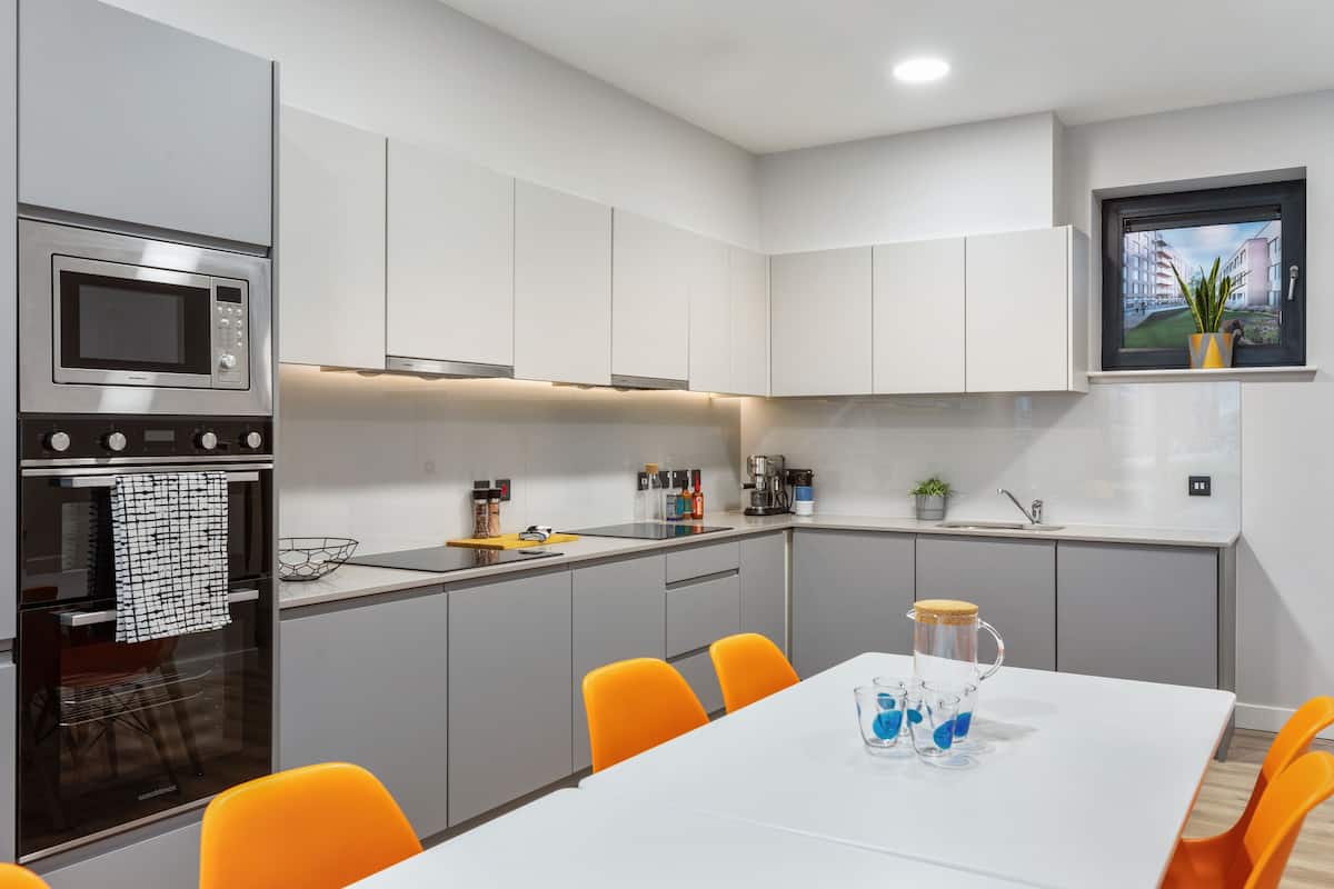 A modern kitchen with white cabinets, a built-in microwave, and a dining area with orange chairs.