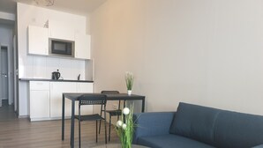 Ein modernes Wohnzimmer mit einem Glastisch, einem blauen Sofa und einem Essbereich mit weißem Tisch und Stühlen.