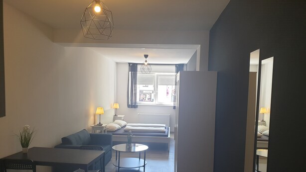 A modern living room with a sofa, two tables, a coffee table, and a hanging light fixture. - Shivas City Aparthotel (Cologne)