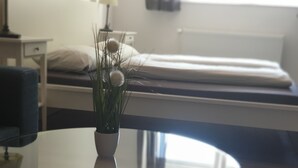 Ein modernes Hotelzimmer mit Glastisch, einem Bett mit weißer Bettwäsche und einem Nachttisch mit Lampe.