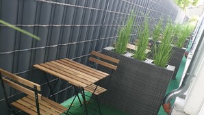 A small outdoor seating area with wooden tables and chairs, a black woven partition, and green artificial turf. - Shivas City Aparthotel (Cologne)