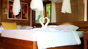 A bed with a heart-shaped towel arrangement, wooden headboard, and a painting on the wall.