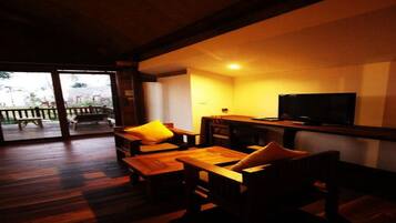 A cozy room with a wooden floor, a television on a stand, and a large window with a view of the outdoors.
