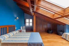 Une chambre avec un plafond en pente, des poutres en bois, un lit avec une literie à motifs, une table de chevet, une chaise et une armoire.