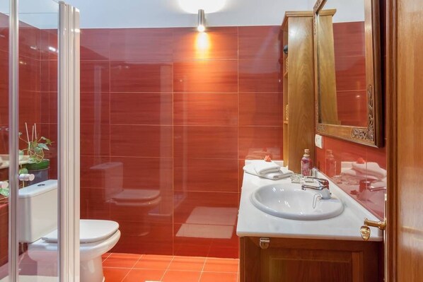Un baño con cabina de ducha de vidrio, un lavabo blanco con grifo dorado y un tocador de madera con espejo.