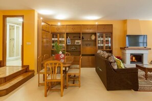 Un salon comprenant un canapé, un téléviseur, une cheminée, une table à manger, des chaises et une bibliothèque.