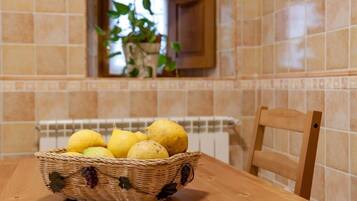 Una cesta de mimbre con limones sobre una mesa de madera en una cocina con paredes de azulejos y una ventana con una planta.