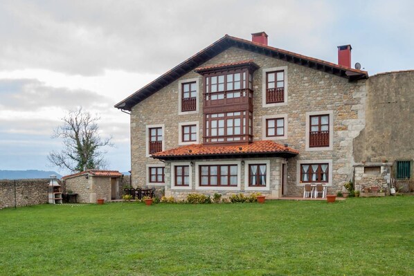 Une maison en pierre avec un toit en tuiles, de nombreuses fenêtres et une pelouse bien entretenue.