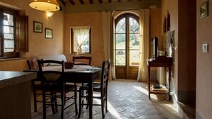 A dining area with a wooden table and chairs, a hanging light fixture, and a view through a window with curtains. - NOBLE FARM HOLIDAY APARTMENT (Montepulciano Siena)