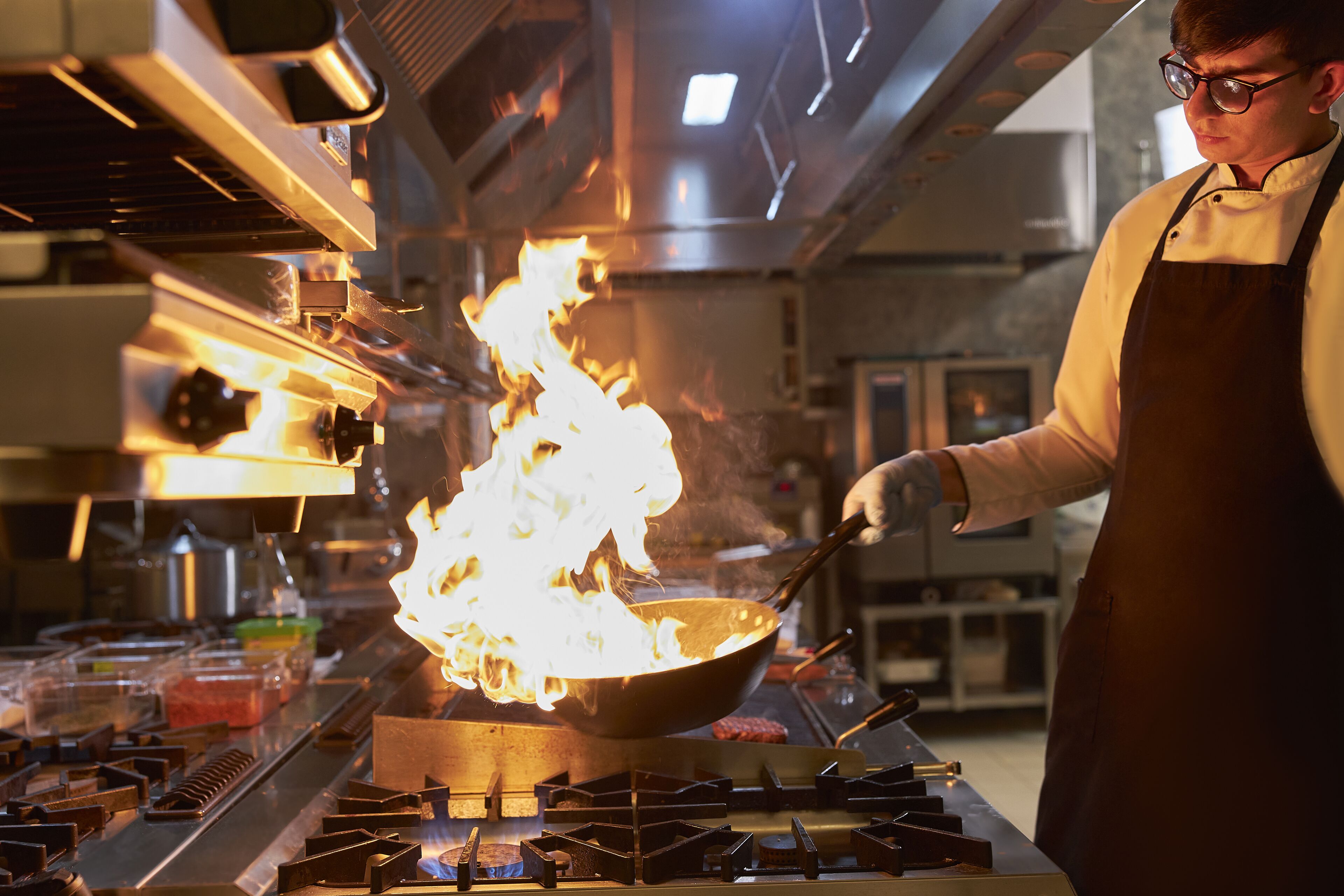 Un chef cuisinant avec un wok enflammé sur un réchaud professionnel dans une cuisine.