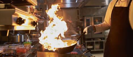 Un chef cuisinant avec un wok enflammé sur un réchaud professionnel dans une cuisine.