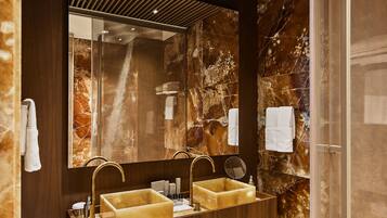 A modern bathroom with a wooden vanity, two sinks, a large mirror, and marble walls.