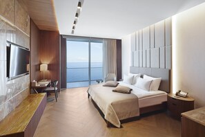 A modern hotel room with a large bed, a desk, and a view of the sea.