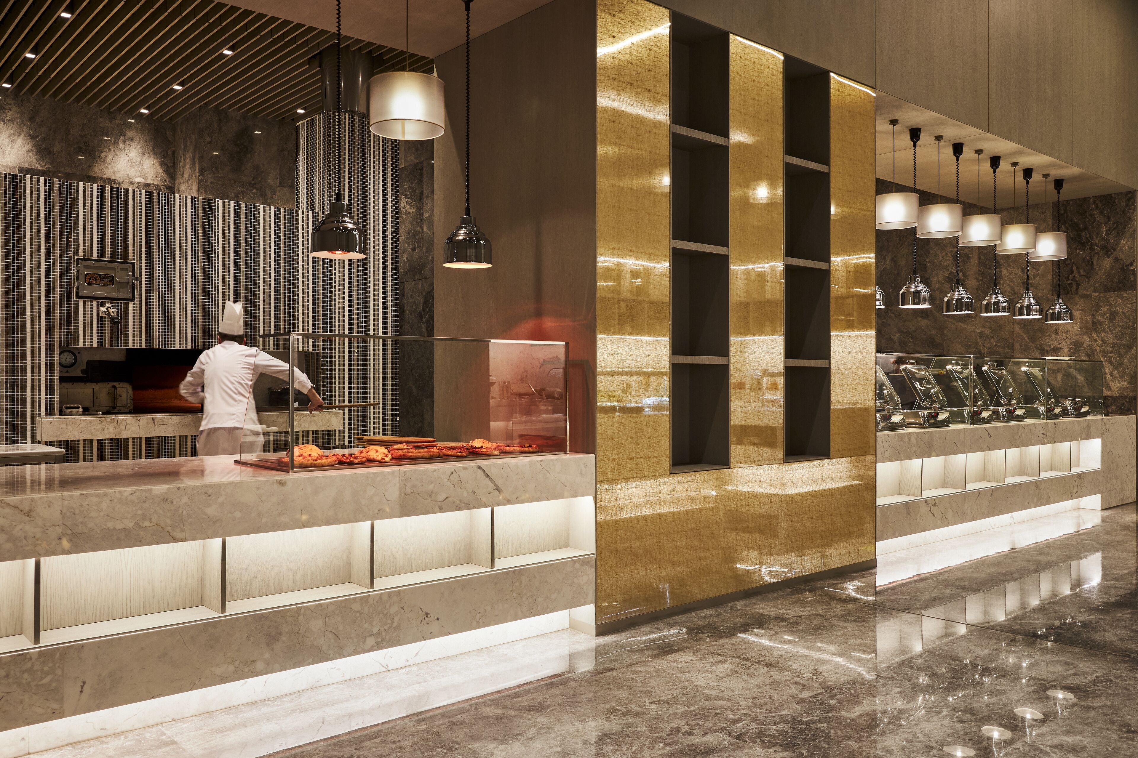 Une cuisine moderne où un chef prépare des plats, avec un plan de travail en marbre et des luminaires suspendus.