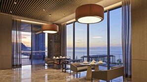 A modern dining area with a view of the sea, featuring a table set for two, large pendant lights, and a polished marble floor. - Ricosta Hotel (Rize)