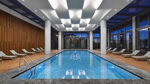 An indoor swimming pool with a checkered pattern on the floor, surrounded by lounge chairs and a wooden wall. - Ricosta Hotel (Rize)