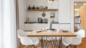 A modern kitchen with a wooden table, white chairs, and a hanging light fixture.