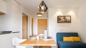 A modern kitchen with a wooden table, white chairs, and a blue sofa with yellow cushions.
