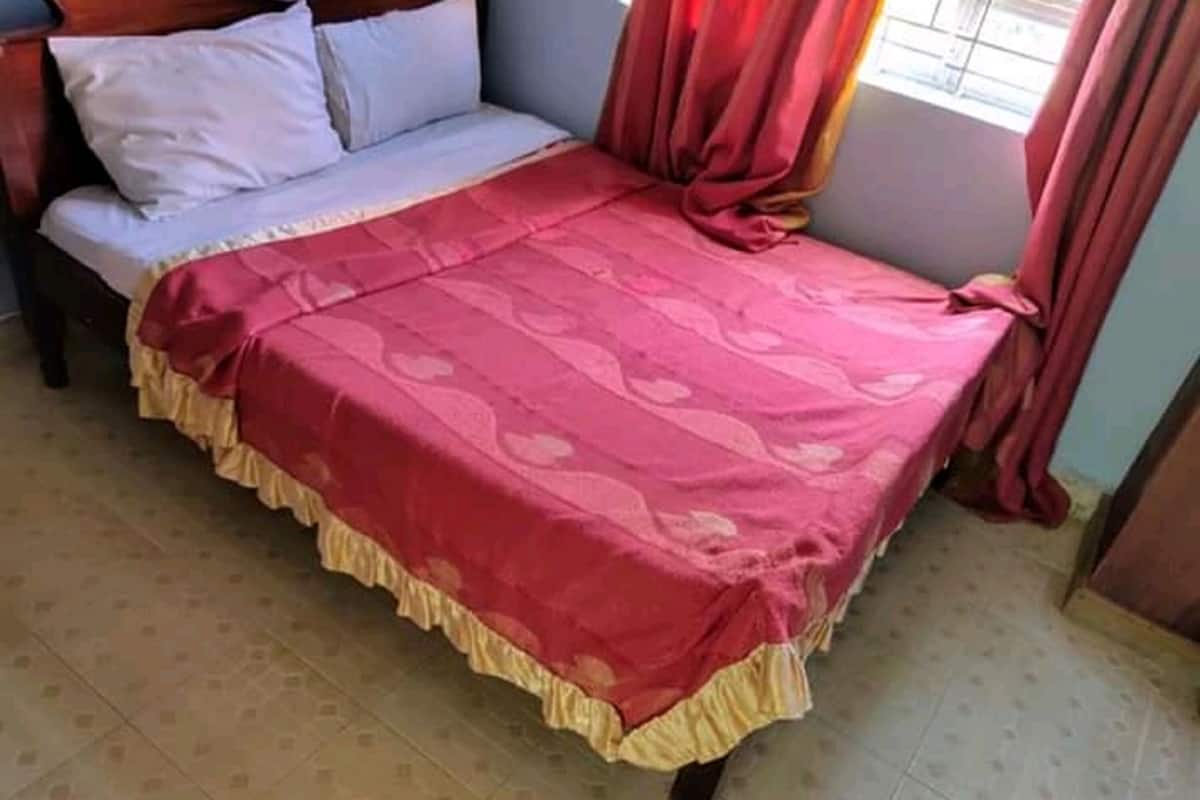 A bedroom with a bed, pillows, a red bedspread, curtains, and a window.