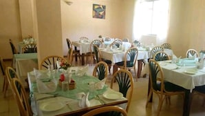 A dining area with multiple tables set for service, chairs arranged around them, and a painting on the wall.
