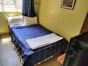 A small bedroom with a bed, a television, and a window with curtains. - Guest House Inn (Nairobi)