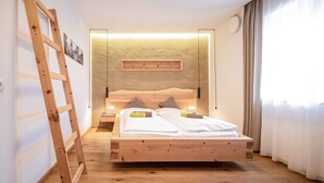Een houten bed met twee kussens en een nachtkastje, een houten ladder en een wandplank met een foto.
