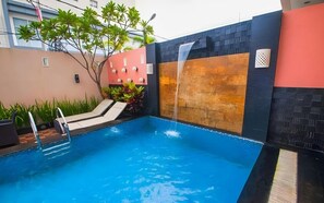 A swimming pool with a waterfall feature, surrounded by a low wall with a mix of brick and stone textures. - Daima Hotel (Padang)
