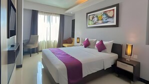 A modern hotel room with a large bed, bedside tables, a desk, a chair, and a painting on the wall. - Daima Hotel (Padang)