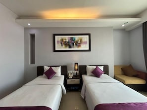 A hotel room with two beds, a bedside table with a lamp, a framed artwork on the wall, and a sofa. - Daima Hotel (Padang)