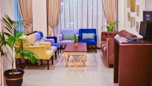 A living room with a sofa set, a coffee table, and a TV on a wooden stand. - Daima Hotel (Padang)