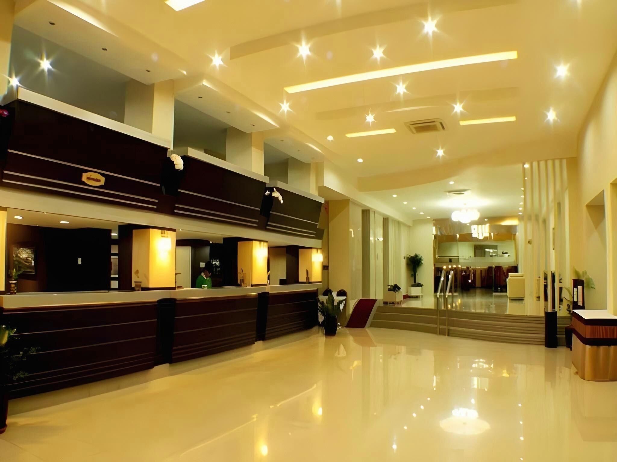 A modern hotel lobby with a reception desk, a staircase, and a large mirror.