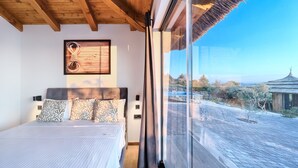 Une chambre avec un grand lit, un plafond en bois, un tableau encadré au mur et une vue sur une cour intérieure avec un bâtiment traditionnel.